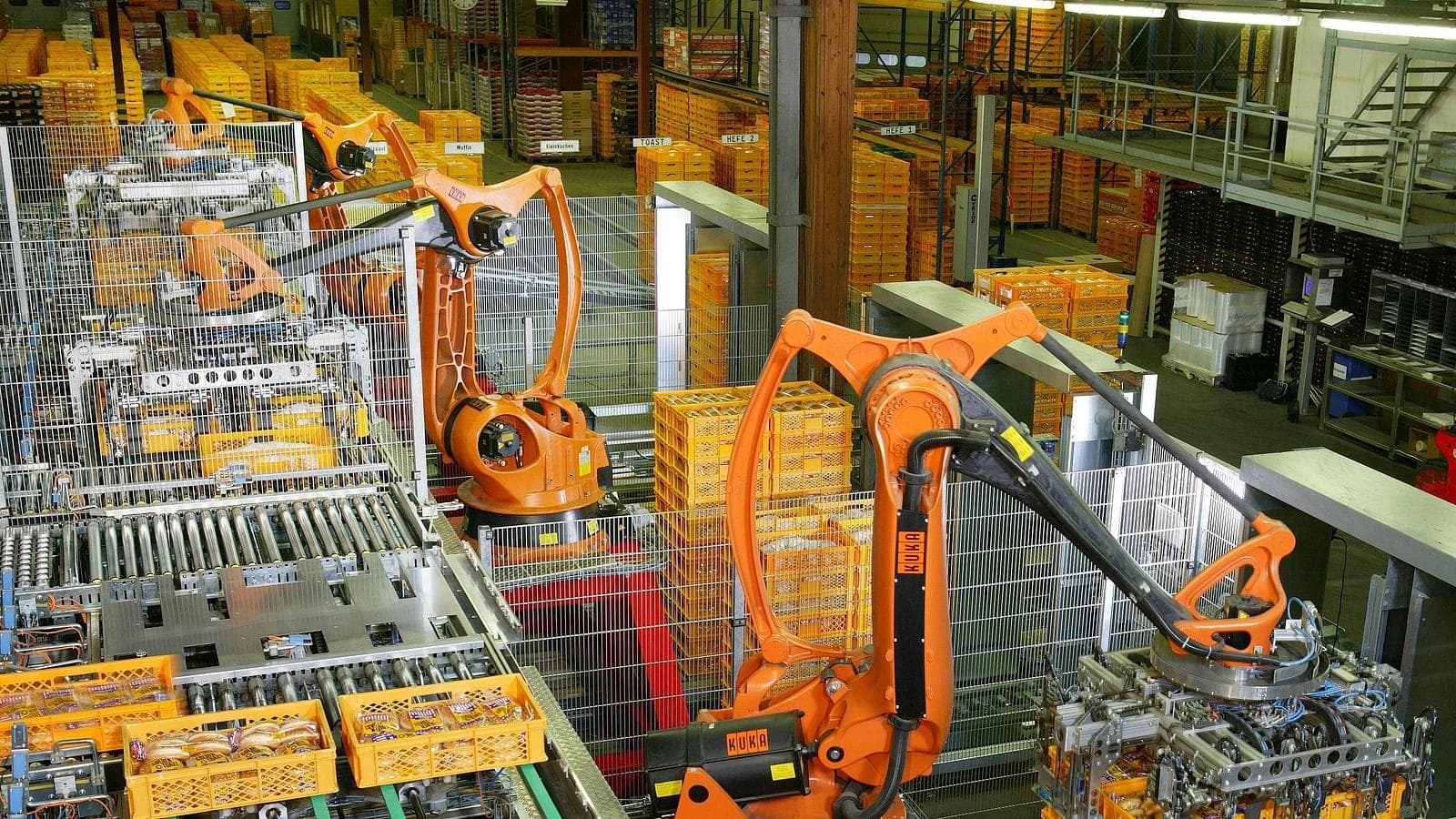 Industrial robot arms palletizing packaged goods in an automated bakery.